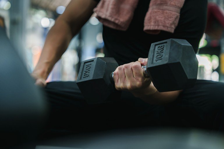 A close-up shot of a man's hand firmly holding a 10kg dumbbell during a focused weightlifting session in a modern gym.